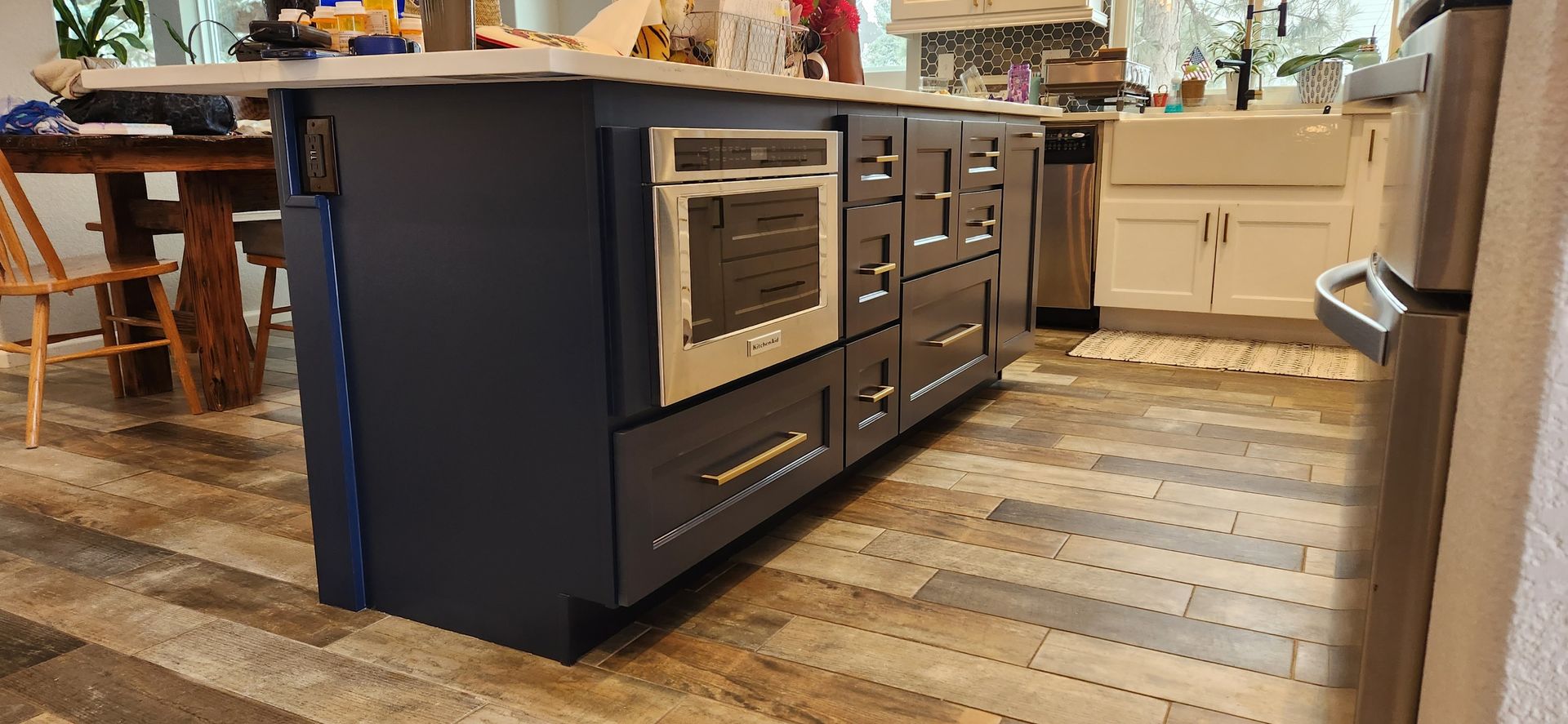 Kitchen island with a built-in oven, drawers, and navy blue cabinetry. Wood-look flooring.