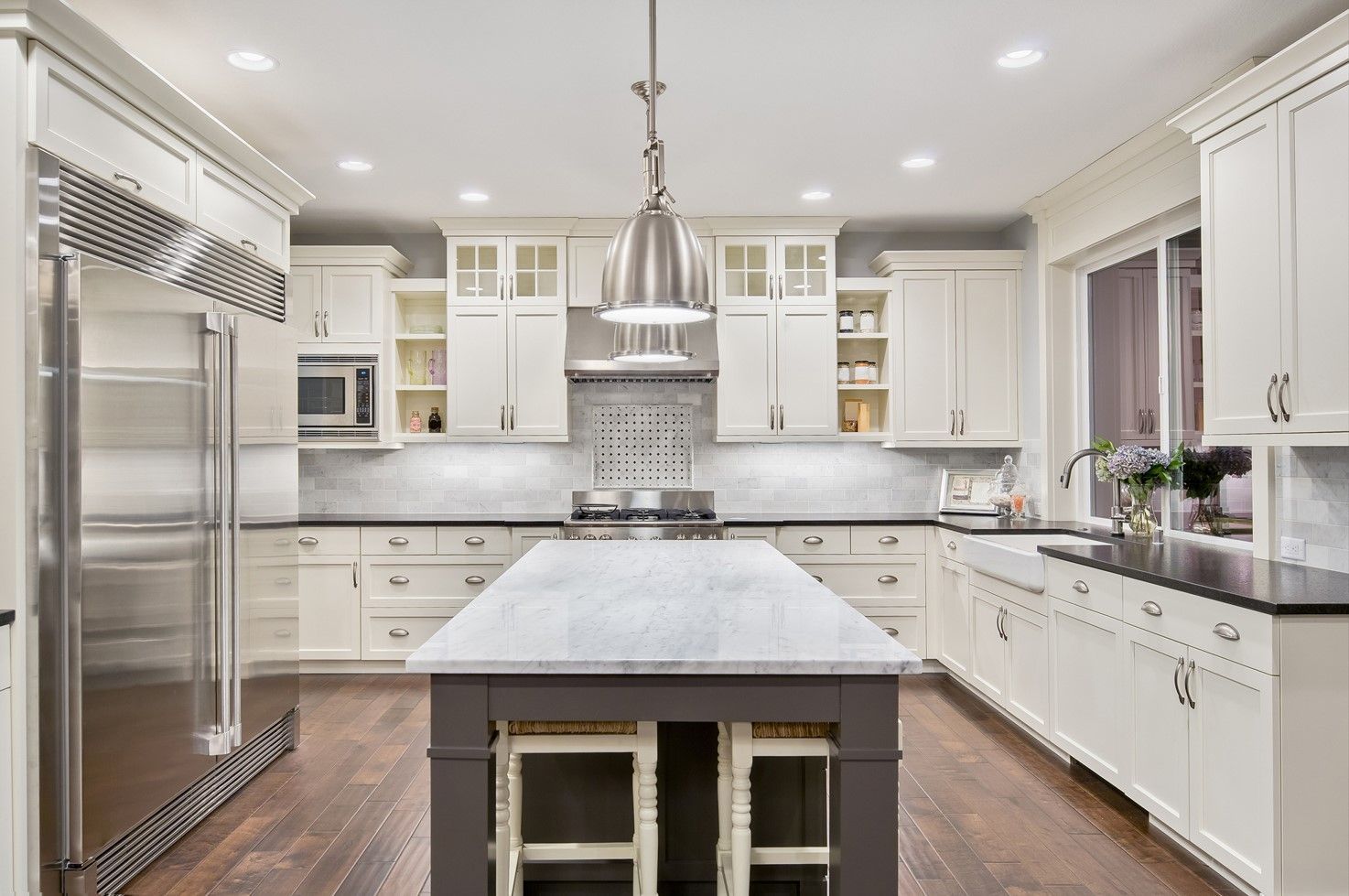 Elegant white kitchen with dark island and hardwood floors, stainless steel appliances.