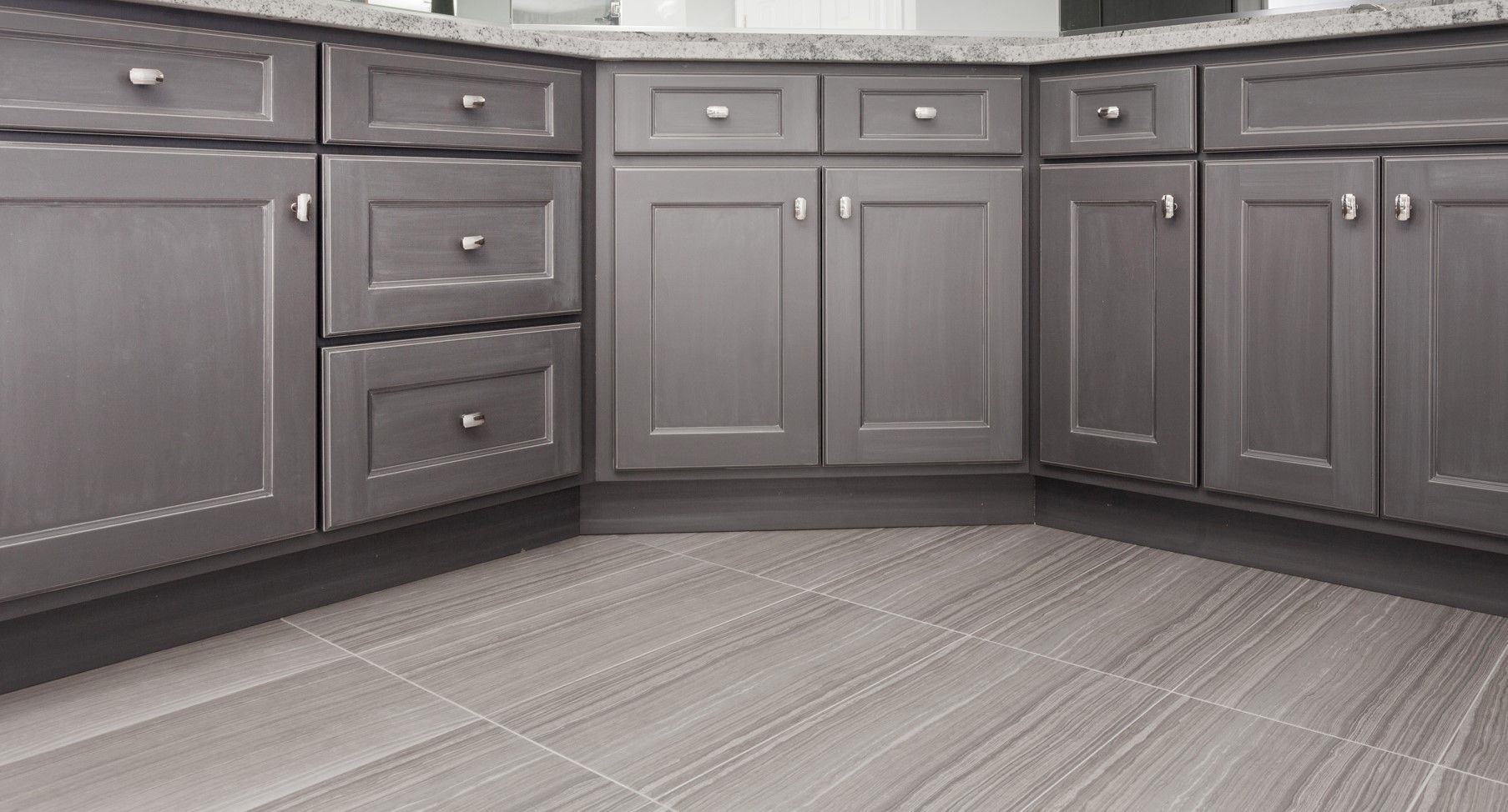 Gray kitchen cabinets with silver hardware and gray tile flooring.
