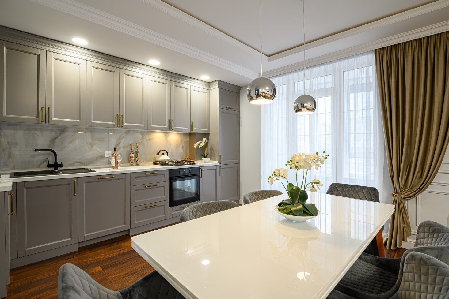 Gray kitchen with marble backsplash, a white dining table, and two chrome pendant lights.