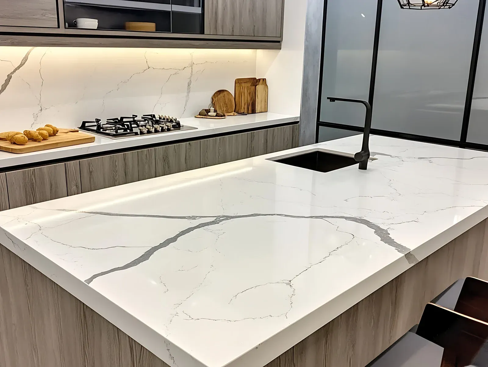 Modern kitchen with white countertop and grey veining, sink, and gas cooktop.