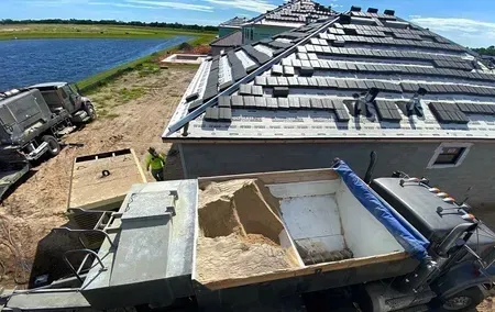 A dump truck filled with sand is parked in front of a house under construction.