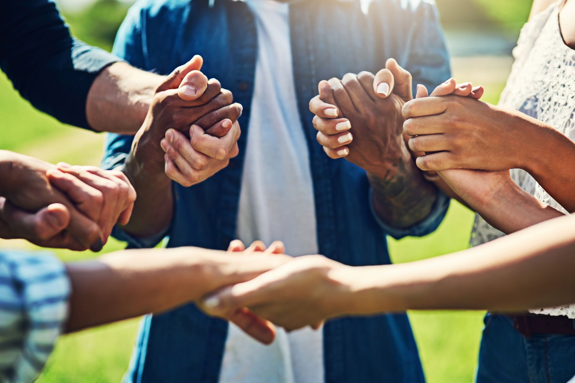 People holding hands in a circle outdoors, representing unity and support.
