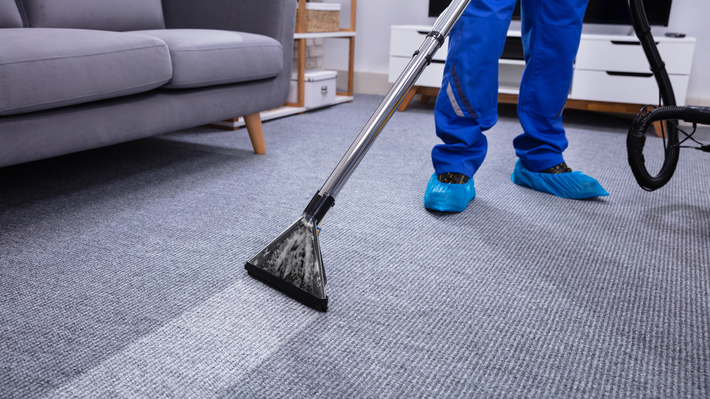 A person is cleaning a carpet with a vacuum cleaner in a living room.