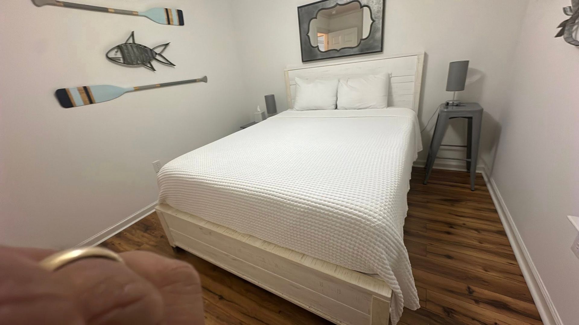 A bedroom with a white bed, oars, fish decoration, and small bedside table.