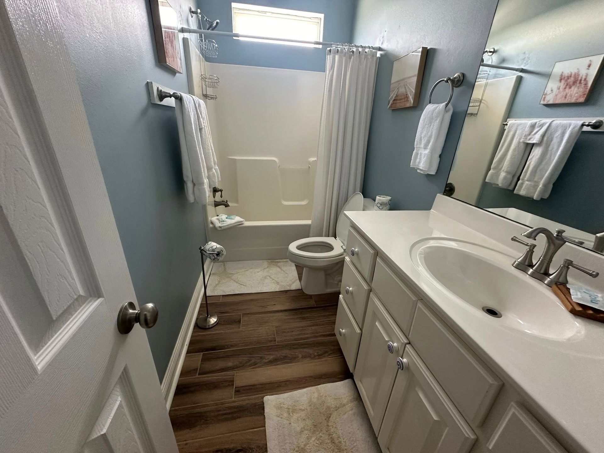 Bathroom with blue walls, white vanity and bathtub, and dark wood-look flooring.