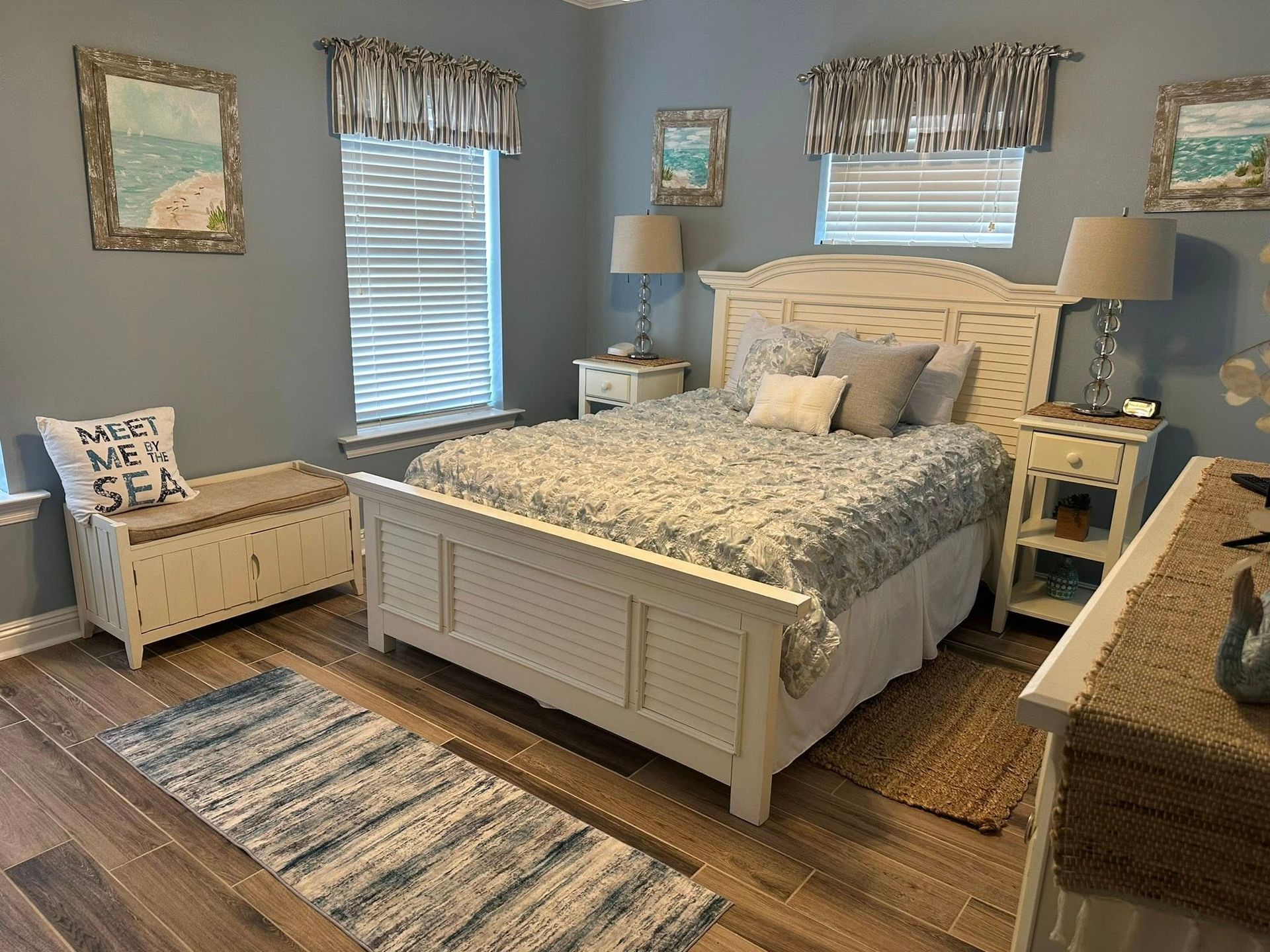Bedroom with blue walls, white furniture, beach-themed decor. Bed, nightstands, chest, window with blinds.