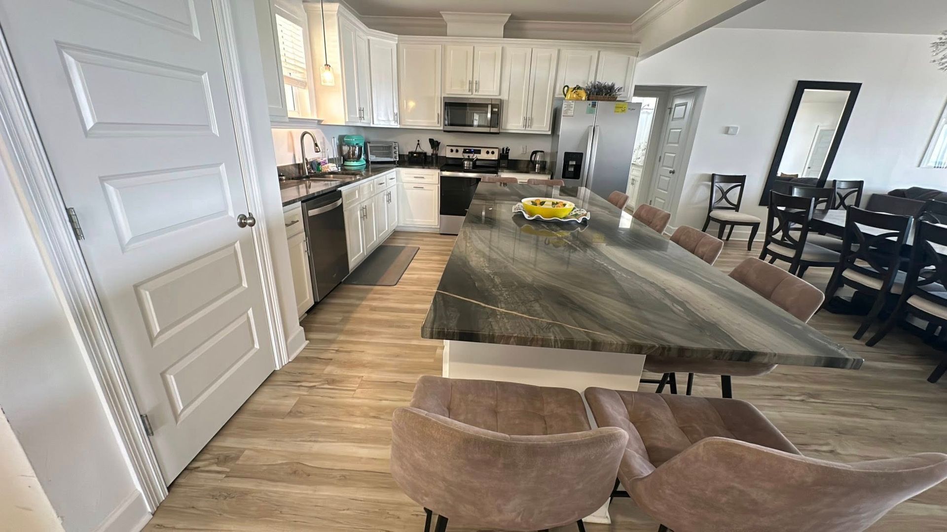 Kitchen with white cabinets, long island with seating, and wood-look flooring.
