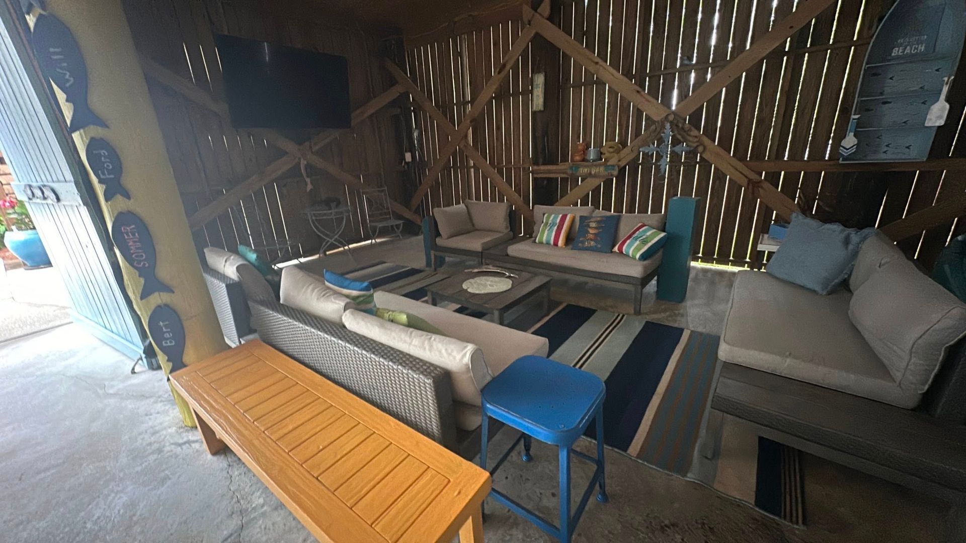 Outdoor seating area with couches, rug, TV, and wooden structure.