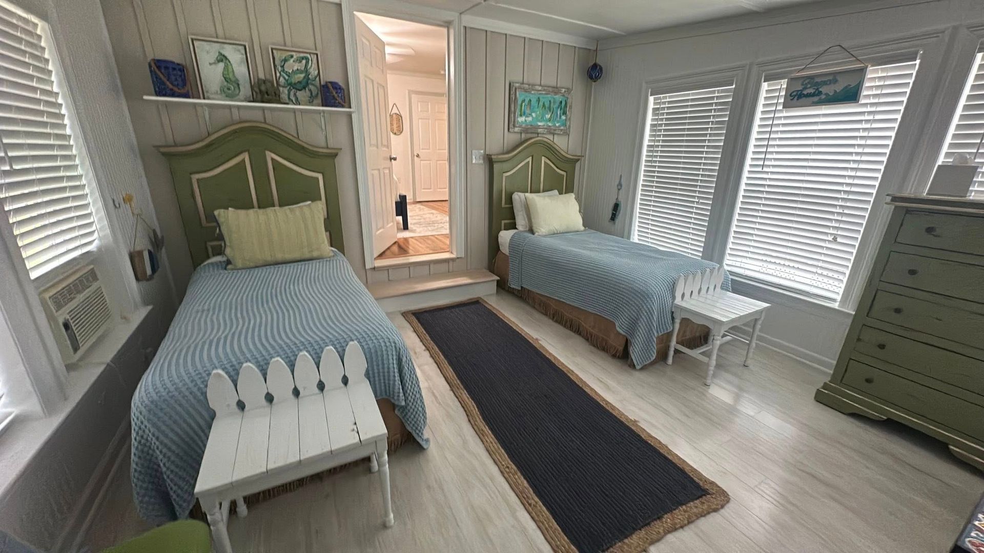 Bedroom with two twin beds, blue and green decor, white shutters and walls.