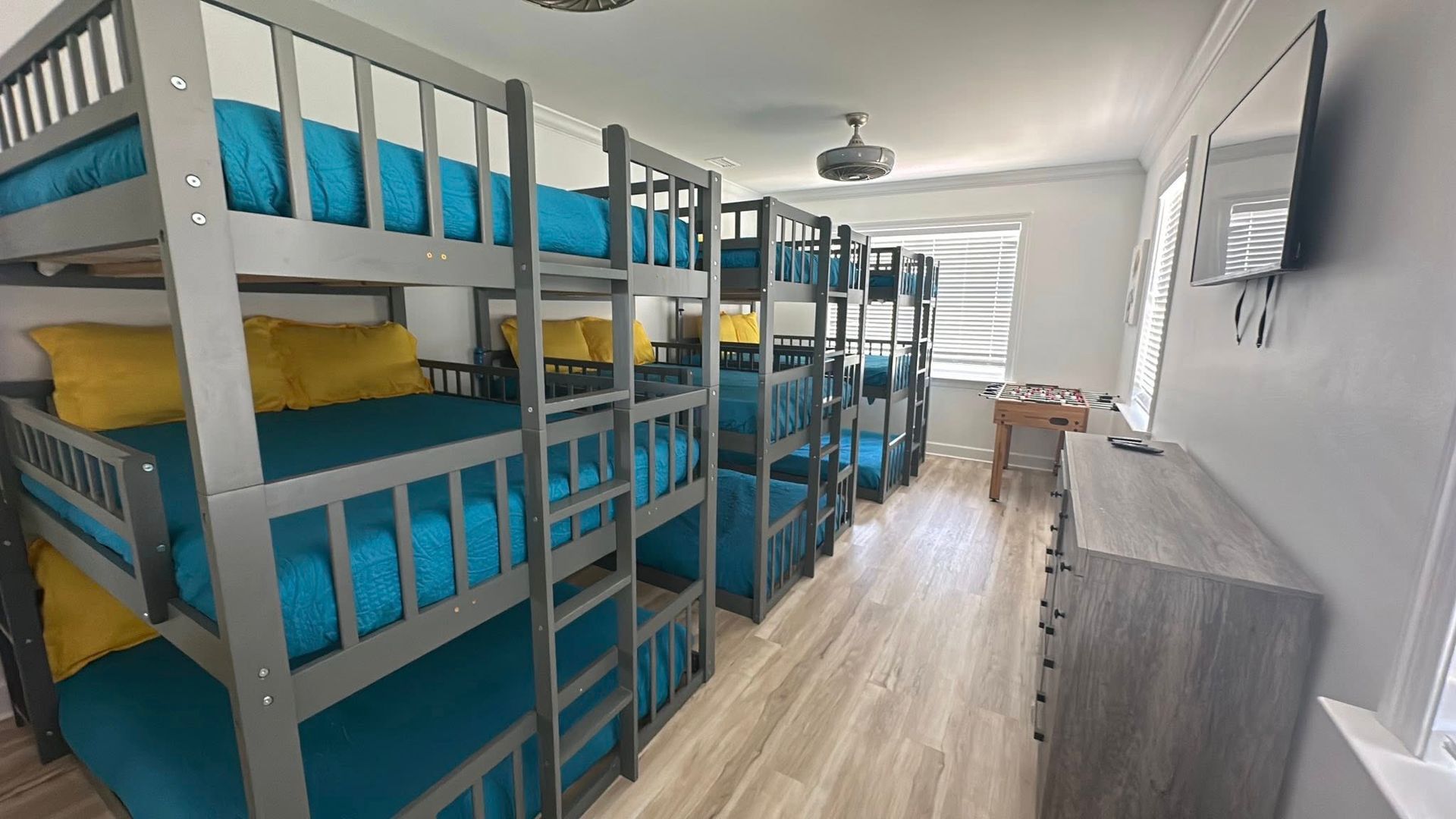 A room with multiple bunk beds. Turquoise bedding, gray frames, and yellow pillows.