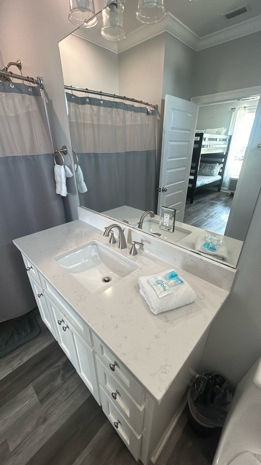 Bathroom with a white vanity, mirror, and gray shower curtain. A bunk bed is visible in the doorway.