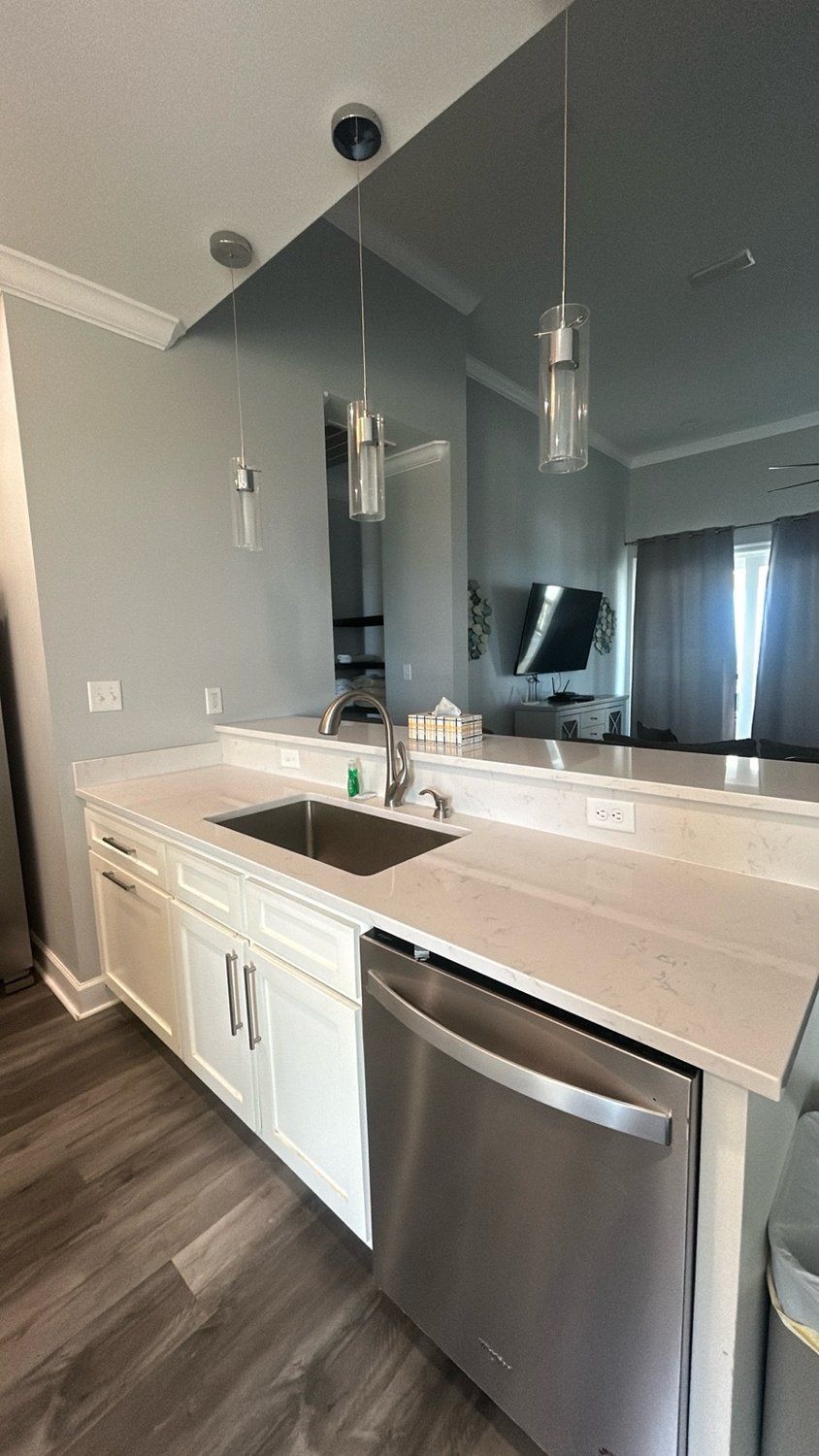 Kitchen with white cabinets, stainless steel dishwasher, and a mirror backsplash.