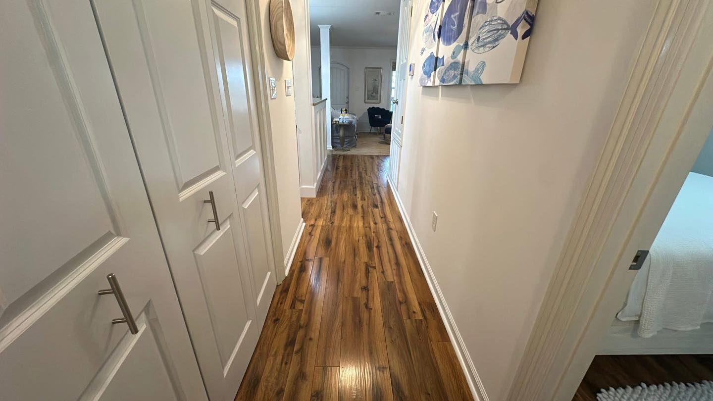Narrow hallway with hardwood floor, white walls, and closed doors.