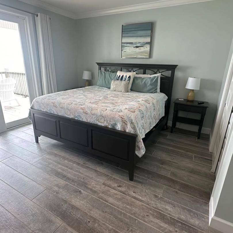 Bedroom with king-size bed, nightstands, and artwork on a light green wall. Sliding glass door to a balcony.