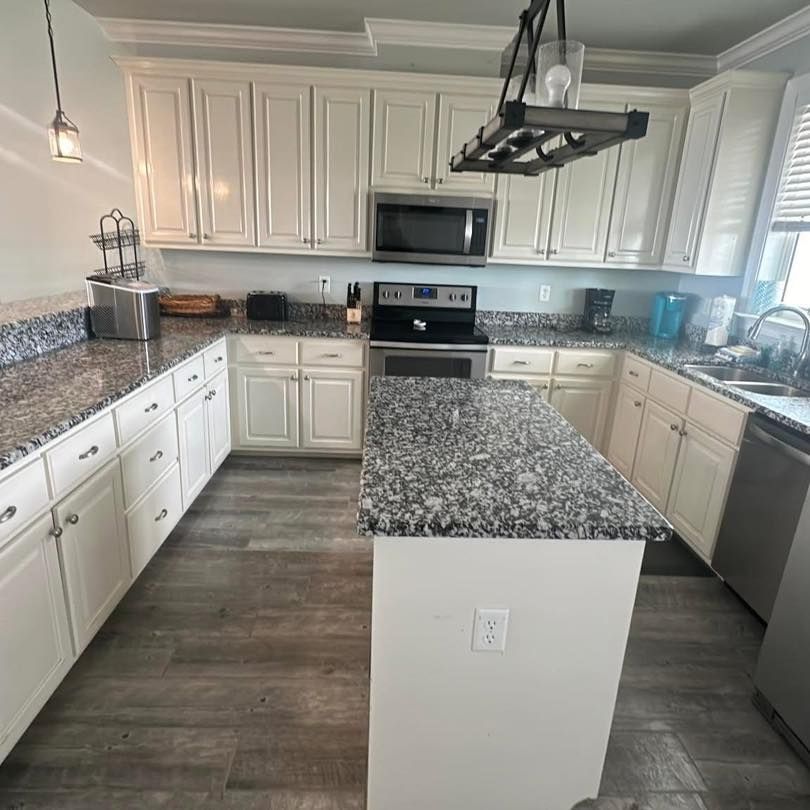U-shaped white kitchen with granite countertops, stainless steel appliances, and wooden flooring.