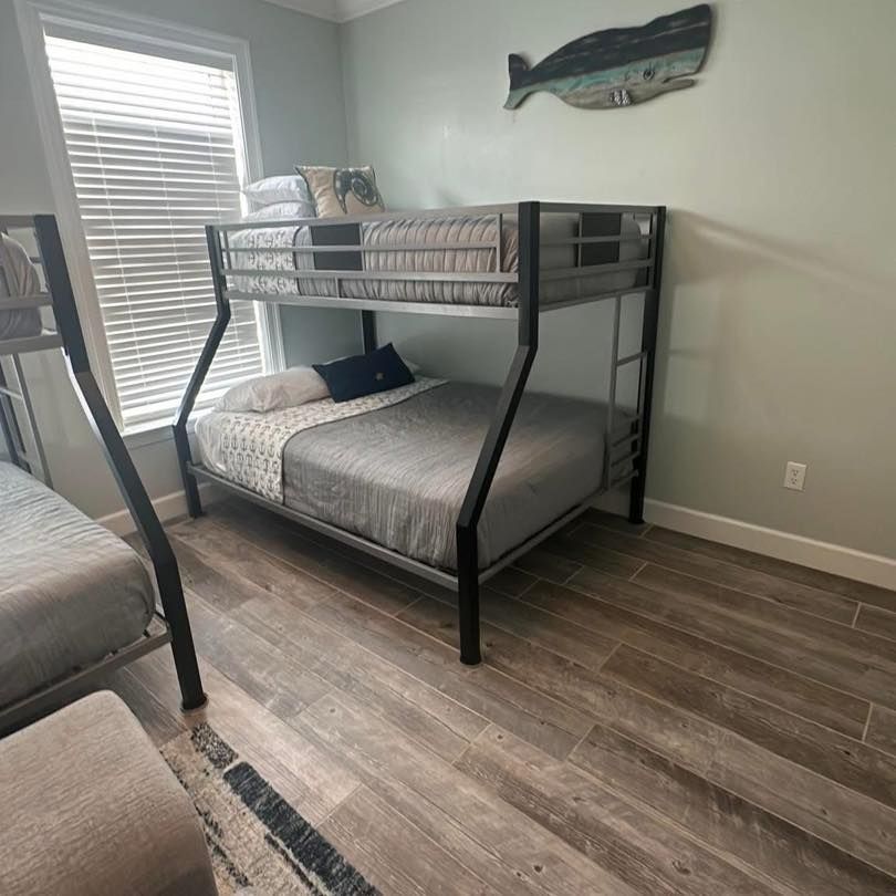 Bunk bed with gray bedding in a bedroom with wooden-look flooring and a window with blinds.