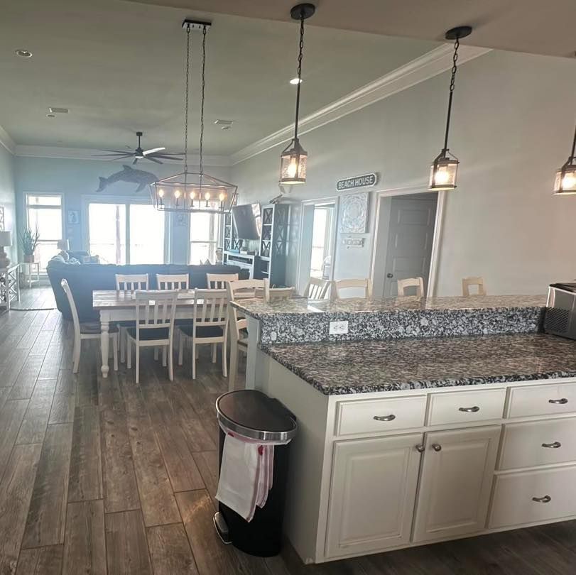 Open-concept kitchen and dining area with granite countertops, wood floors, and hanging lights.