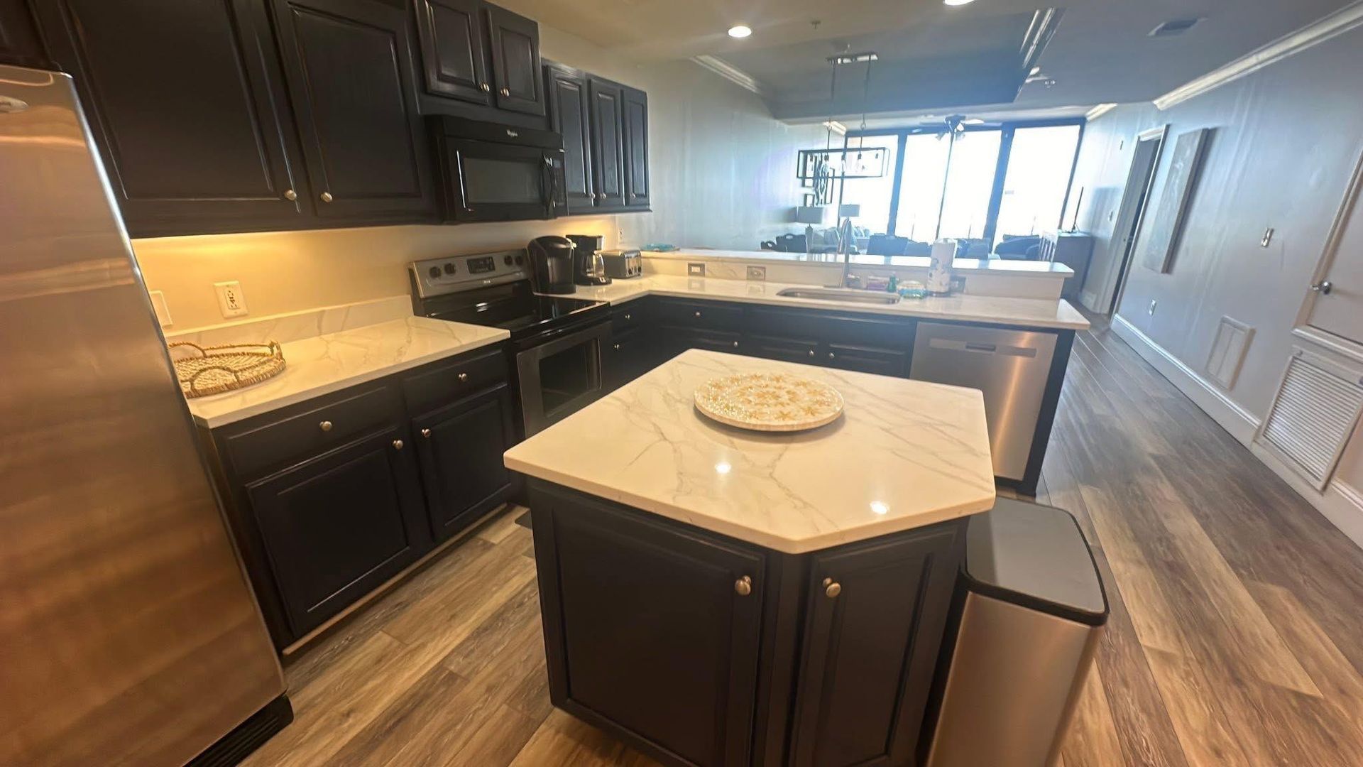 Dark kitchen with stainless steel appliances, white countertops, and island.