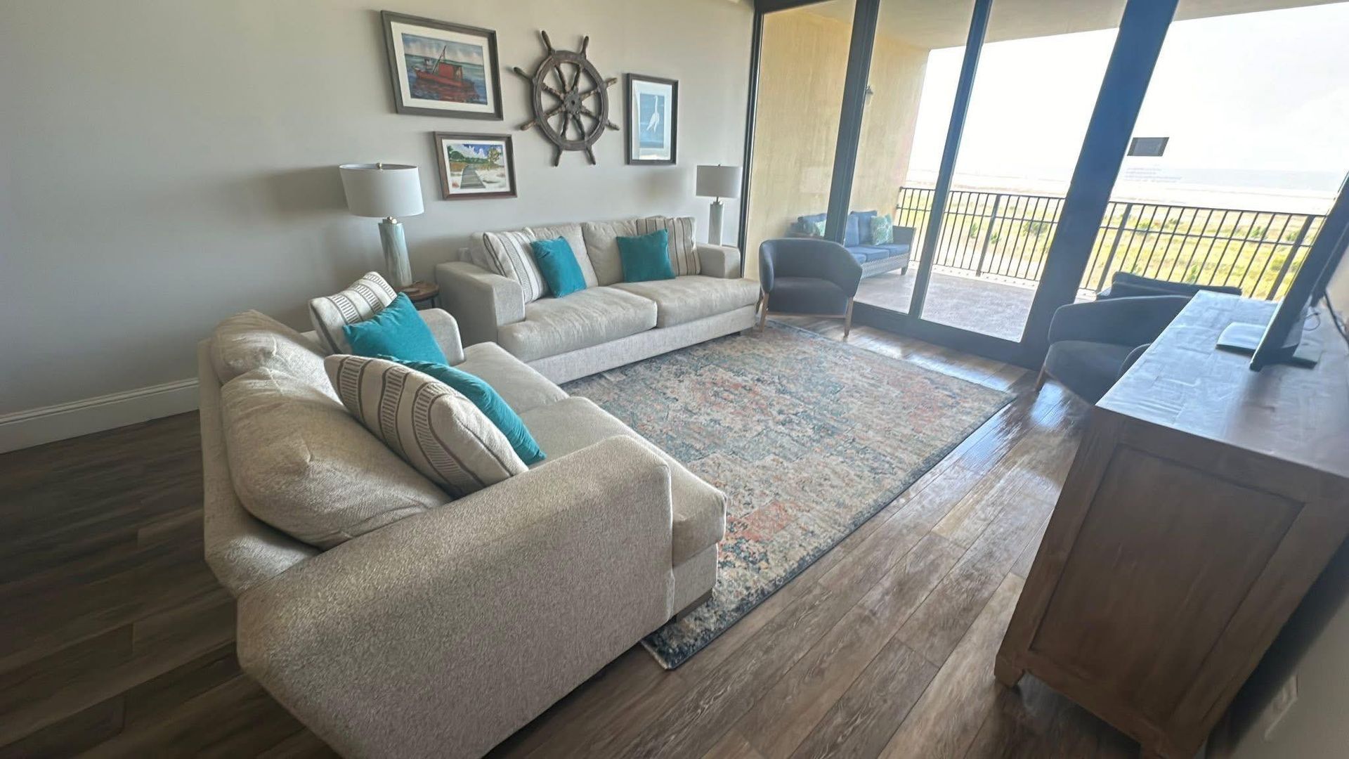 Living room with beige sectional, teal pillows, rug, artwork, and balcony with ocean view.