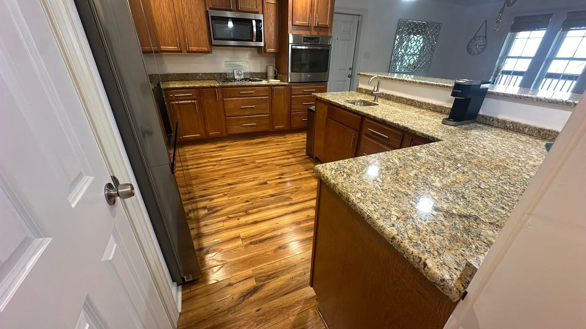 A kitchen with wood cabinets, granite countertops, hardwood floors, and stainless steel appliances.