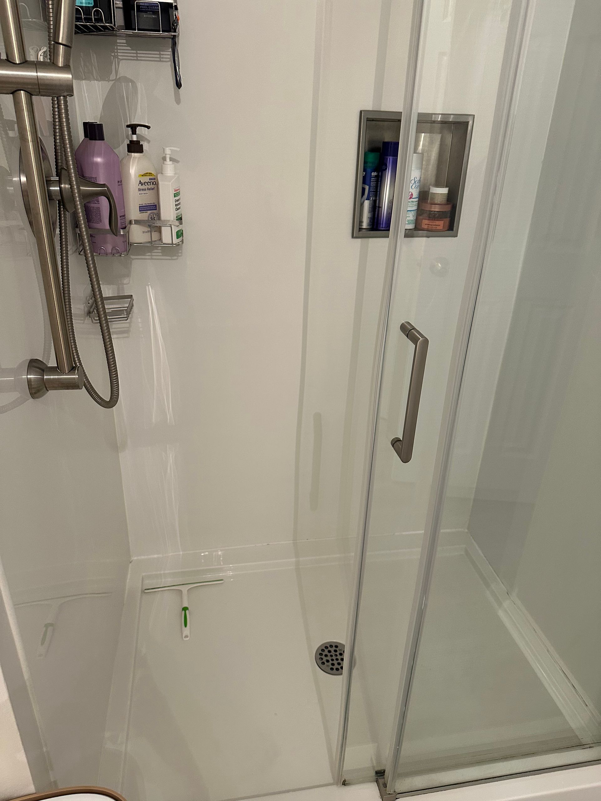 A shower stall with a glass door, a metal shower head, and built-in wall shelving containing various shampoo bottles.