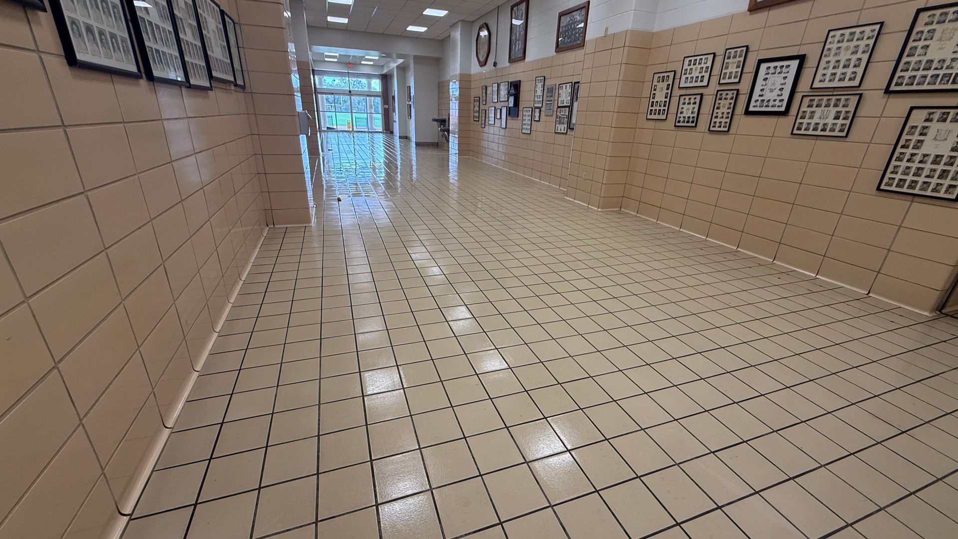 A tiled hallway with cream-colored walls, featuring rows of framed photos and a shiny, grid-patterned floor.