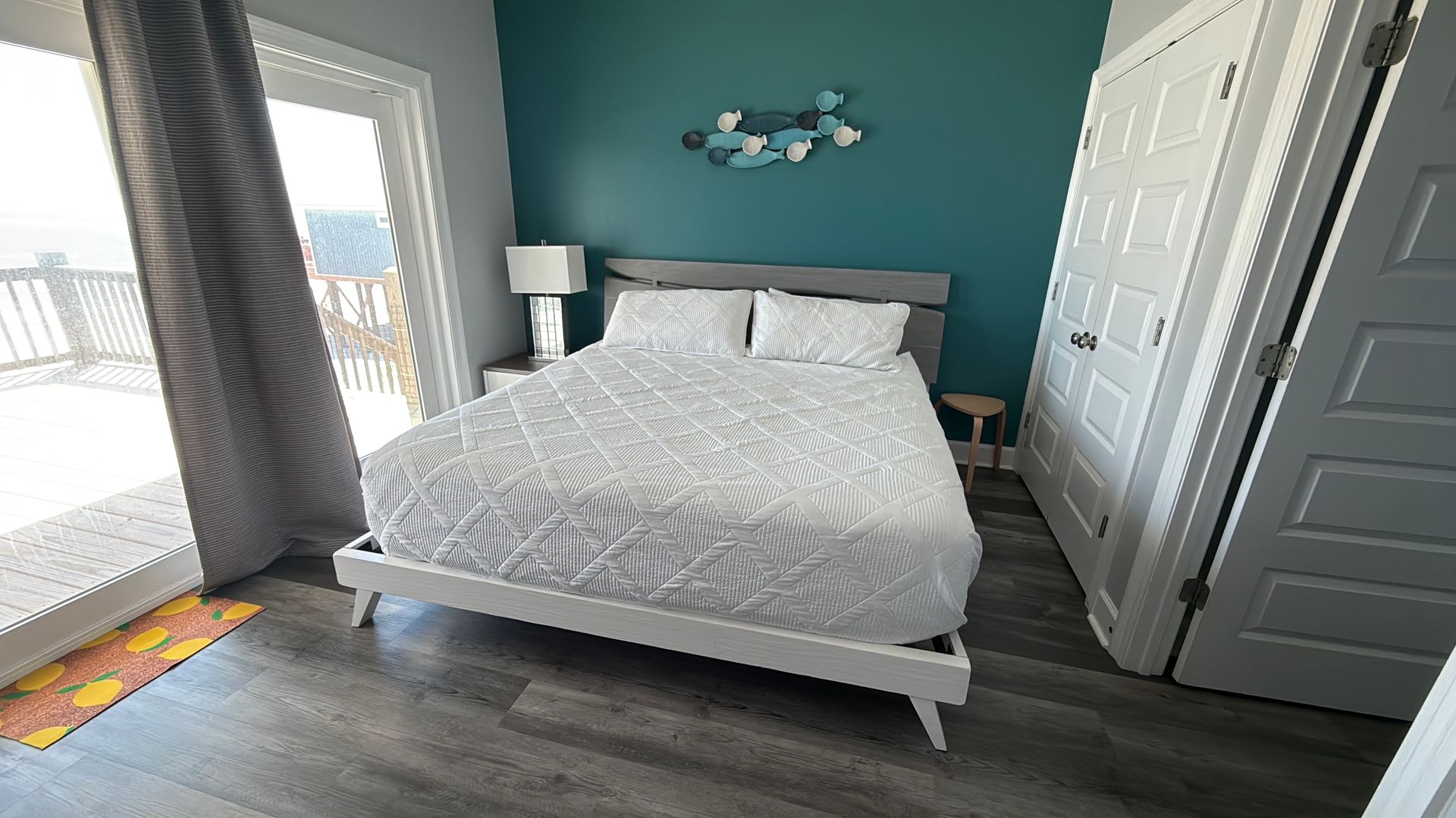 A bedroom featuring a queen bed with a white patterned quilt, teal accent wall, sliding glass doors, and gray floors.