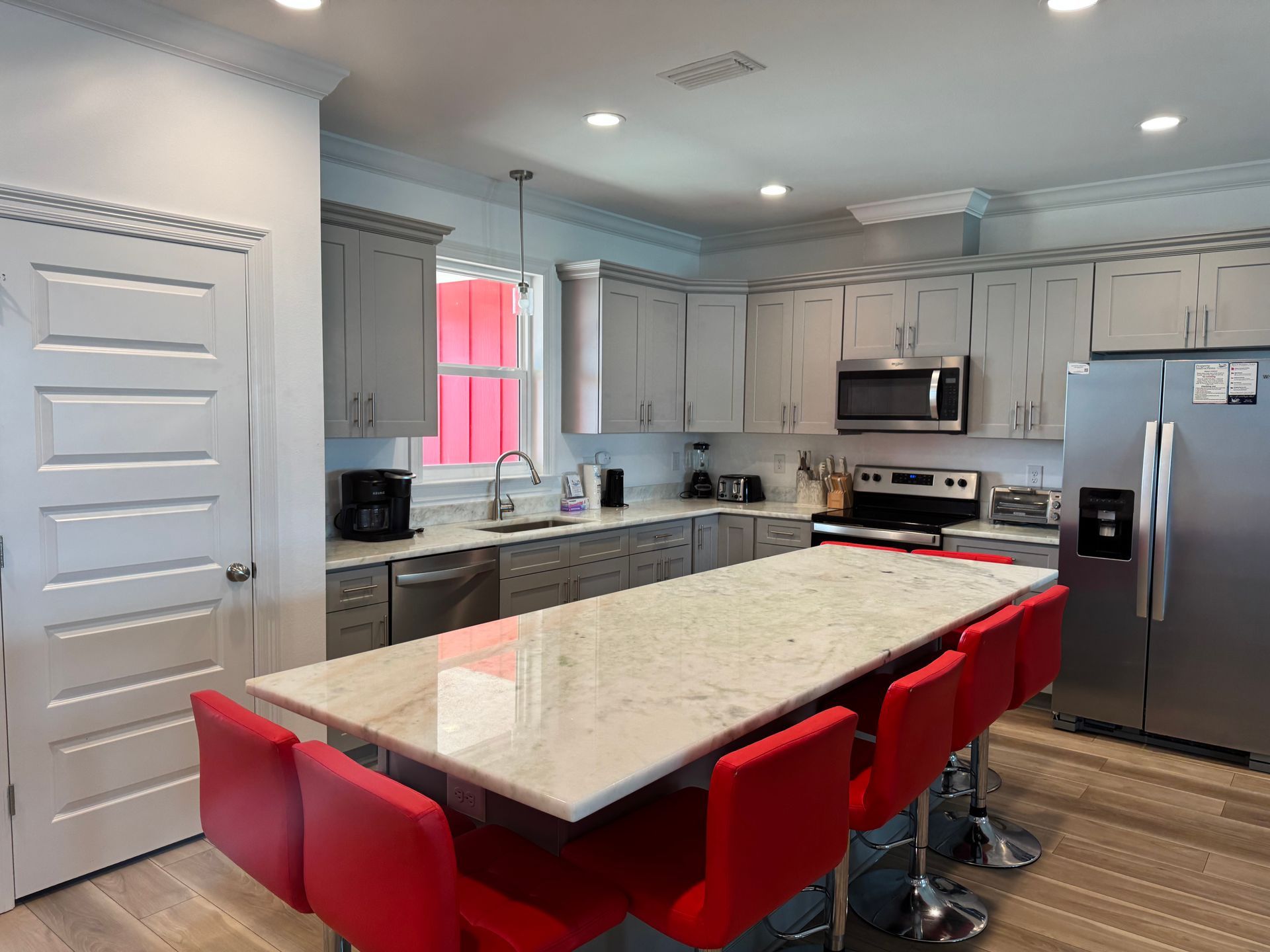A modern kitchen with grey cabinetry, a white marble island, and six bright red stools.