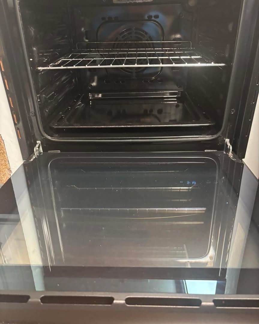 The open door of a clean, black electric oven featuring a wire rack and a baking tray inside.