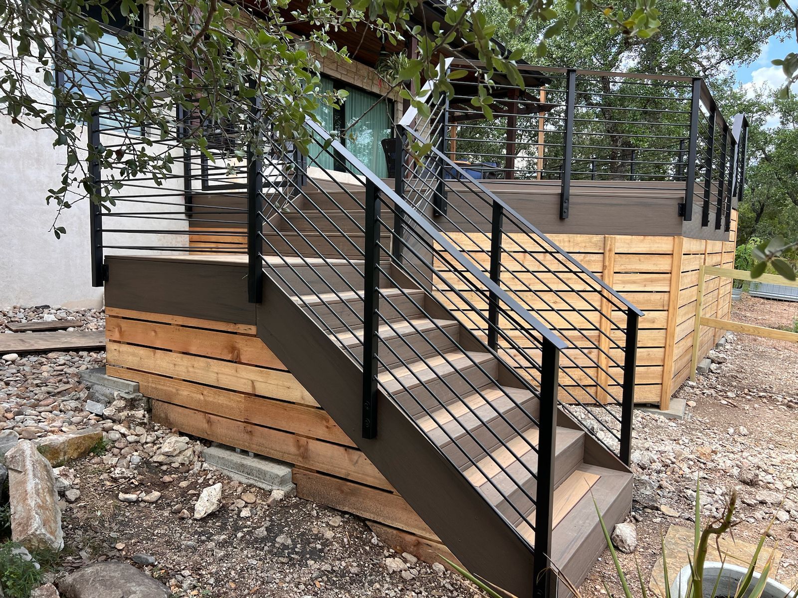 Wooden deck with black railings and steps, surrounded by wood panels.
