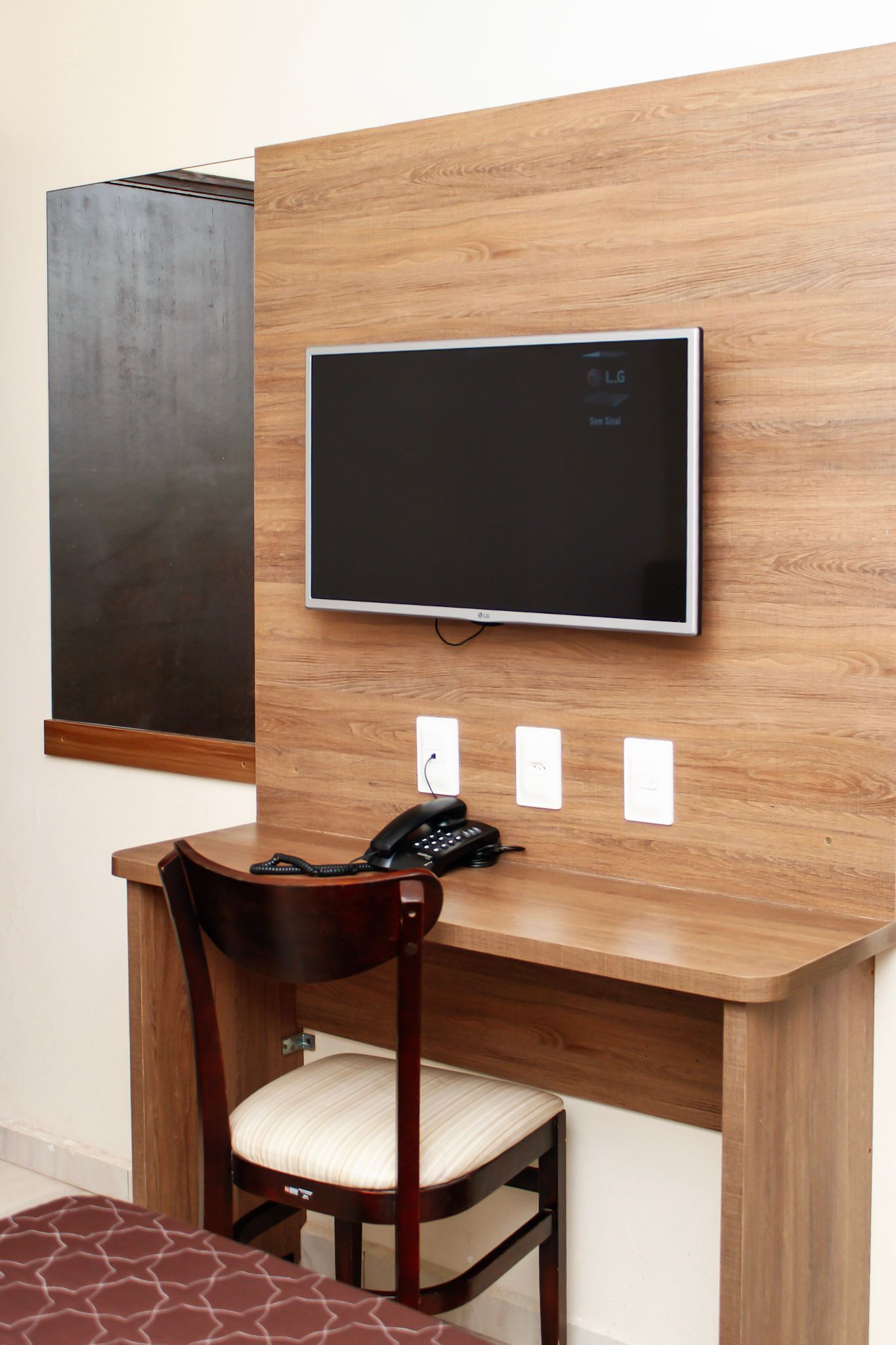 Área de trabalho com TV, telefone, cadeira e tomadas elétricas montadas em uma parede com painéis de madeira.