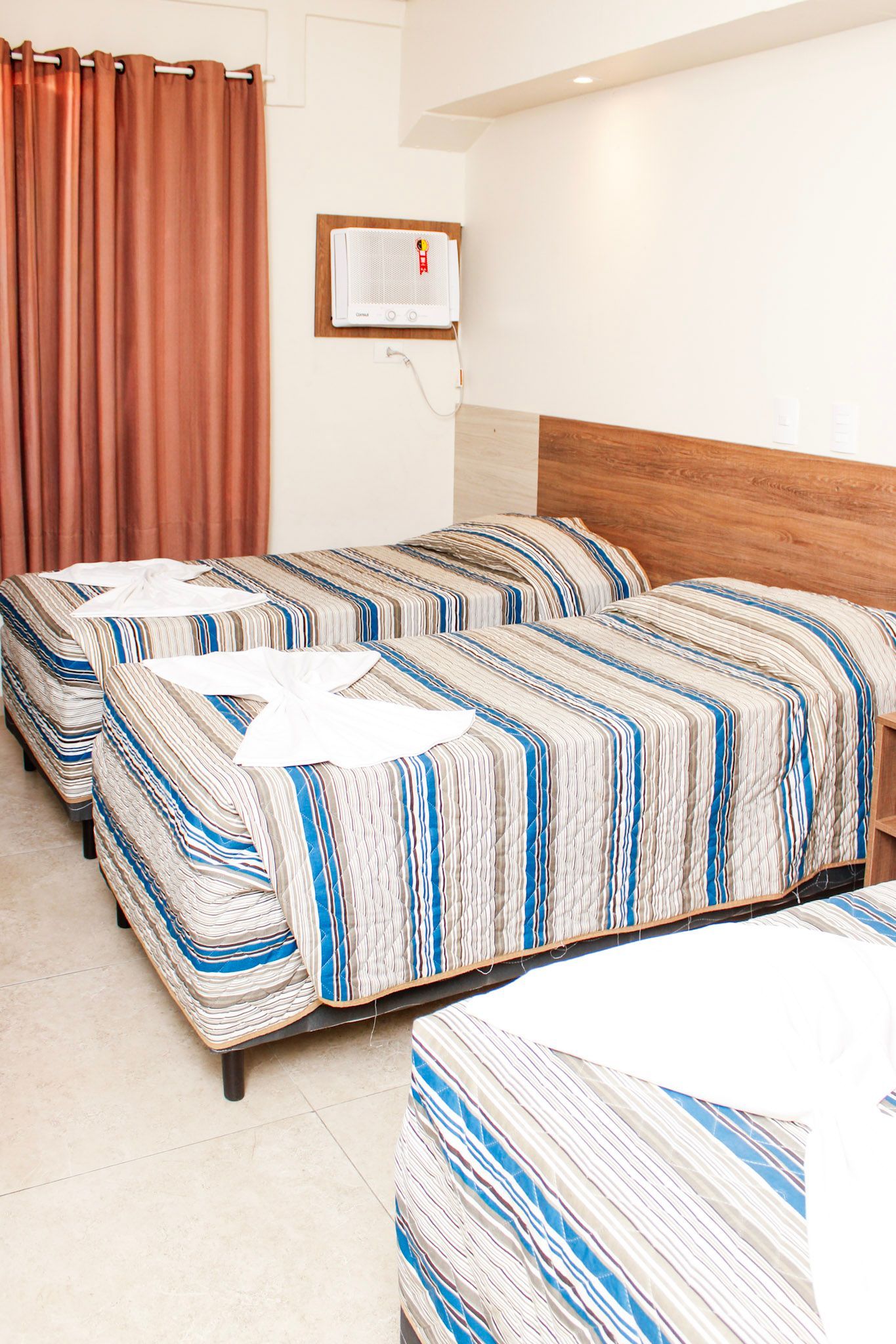 Duas camas de solteiro em um quarto de hotel com cobertores estampados, cortinas marrons e cabeceira.