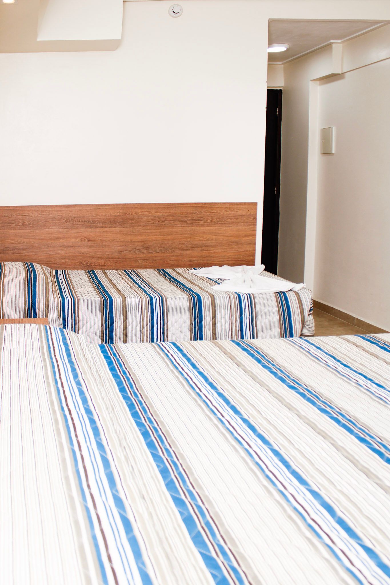 Duas camas com roupa de cama listrada de azul e branco em um quarto simples e bem iluminado.