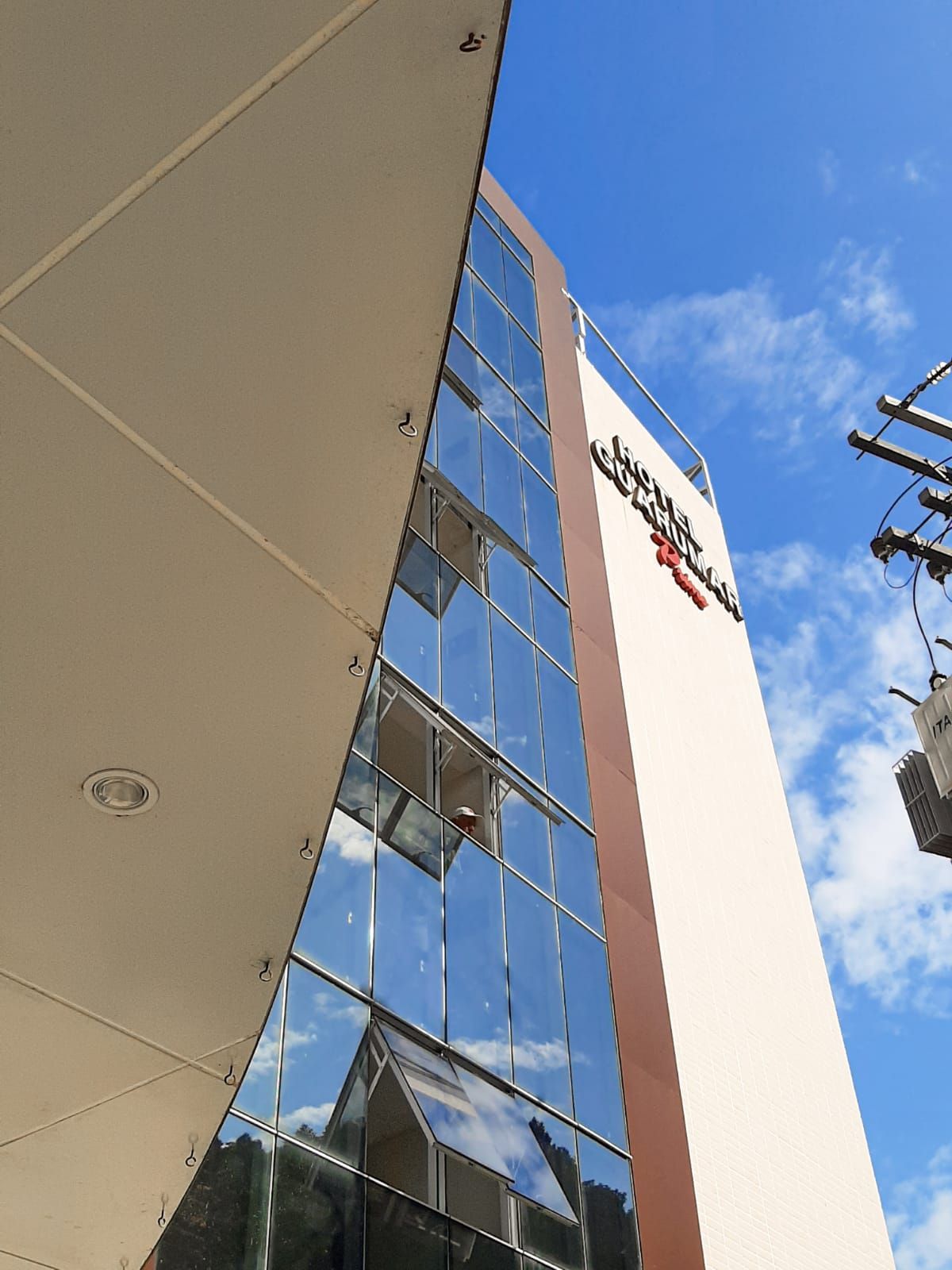 Prédio alto com janelas de vidro, janelas abertas e uma placa contra um céu azul.