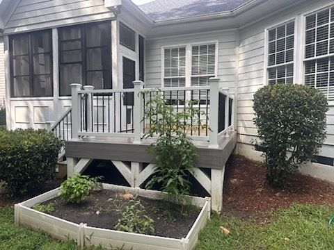 A gray deck with black railings, a garden bed, and a screened porch attached to a light-colored house.