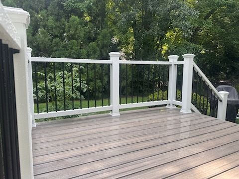 A deck with white railing, black spindles, and gray composite decking overlooks green trees.