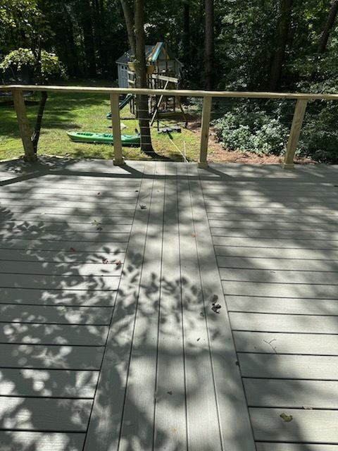 Wooden deck with railing overlooking a green lawn, trees, and a playhouse.