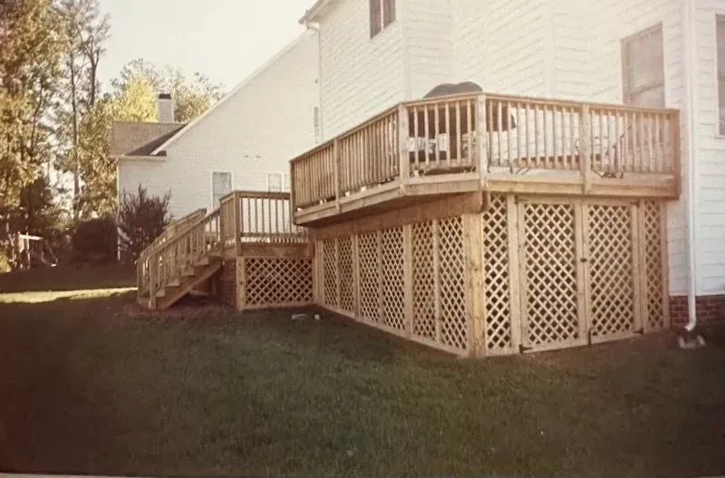 A large wooden deck with stairs is in the backyard of a house.
