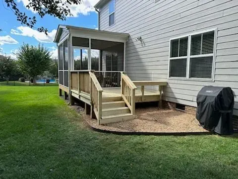 A screened in porch with stairs and a grill in front of a house.