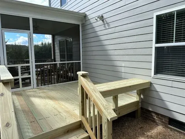 A screened in porch with a wooden deck and stairs leading to it.