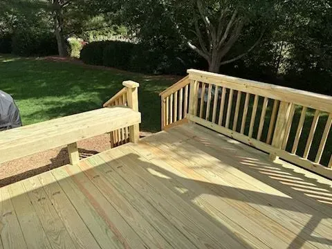 A wooden deck with a bench and stairs in a backyard.