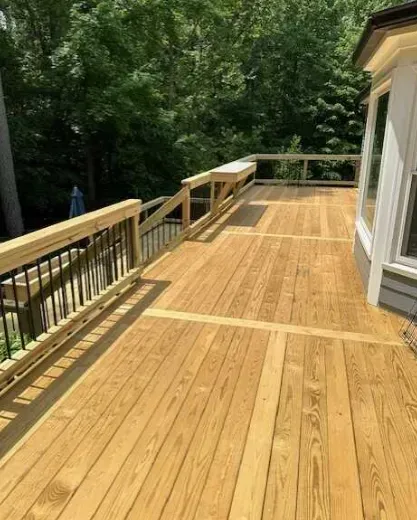 A large wooden deck with a railing and trees in the background.