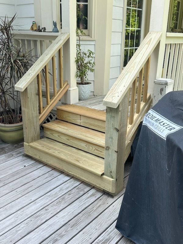 Wooden deck steps with handrails, leading to a porch, with a covered grill nearby.