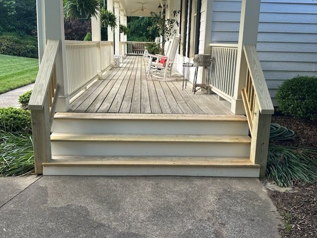 Wooden porch with three steps leading to a house with white siding, railings, and porch posts.