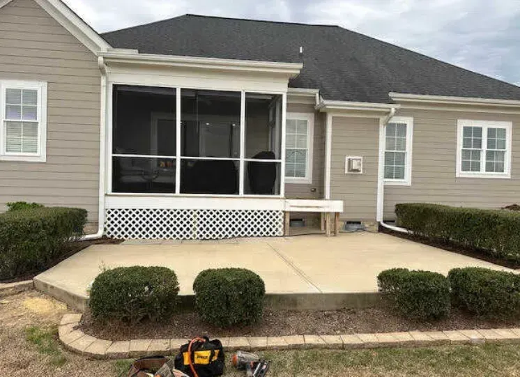 A man is sitting on a patio in front of a house with a screened in porch.
