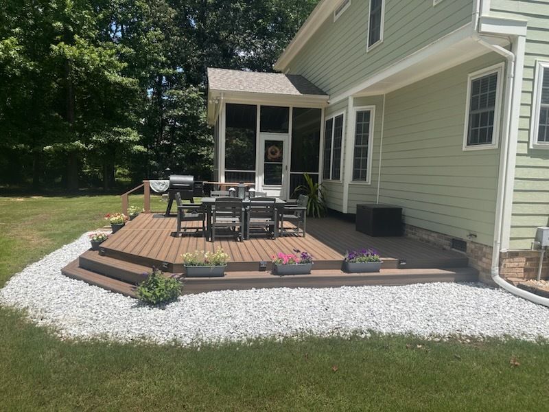 Backyard deck with dining set, steps, white stones, and a screened porch, next to a green house.