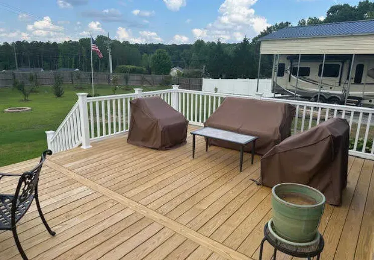 A wooden deck with a couch , chairs , table and potted plant.