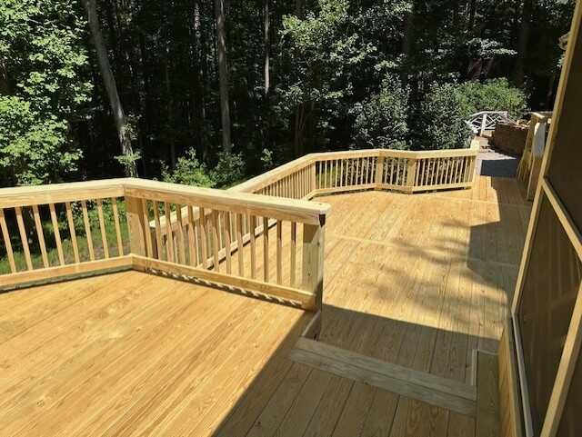 A wooden deck with stairs leading up to it is surrounded by trees.
