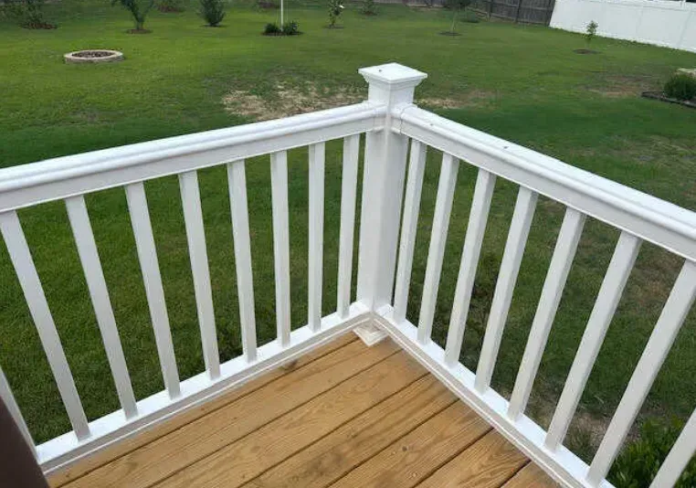 A white railing on a wooden deck overlooking a lush green field.